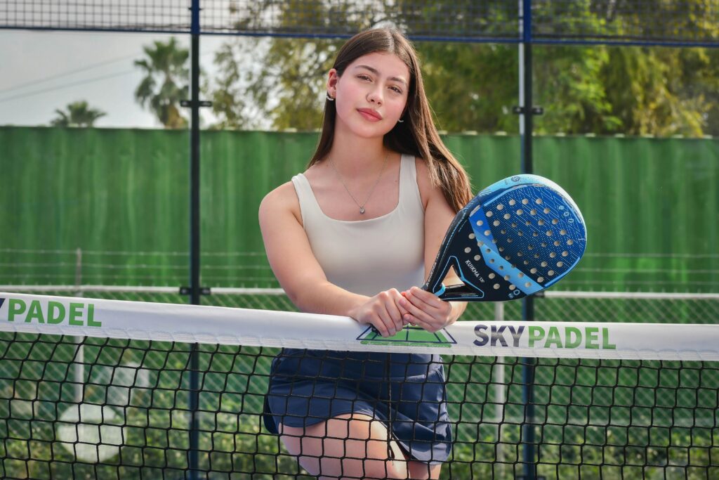 Confident woman holding a padel racket, standing on an outdoor court. Perfect for sports and lifestyle themes.